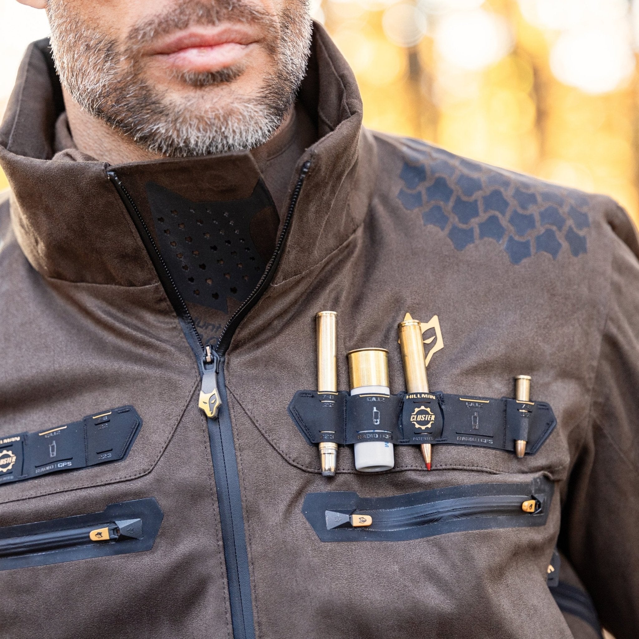 A man wears the HILLMAN GEAR Camo Hunting Jacket 6OL Heated—Cold Weather Insulated—with multiple chest compartments for tools like pens, flashlight, and multitool. Geometric shoulders add to its blend of practicality and rugged outdoor style.
