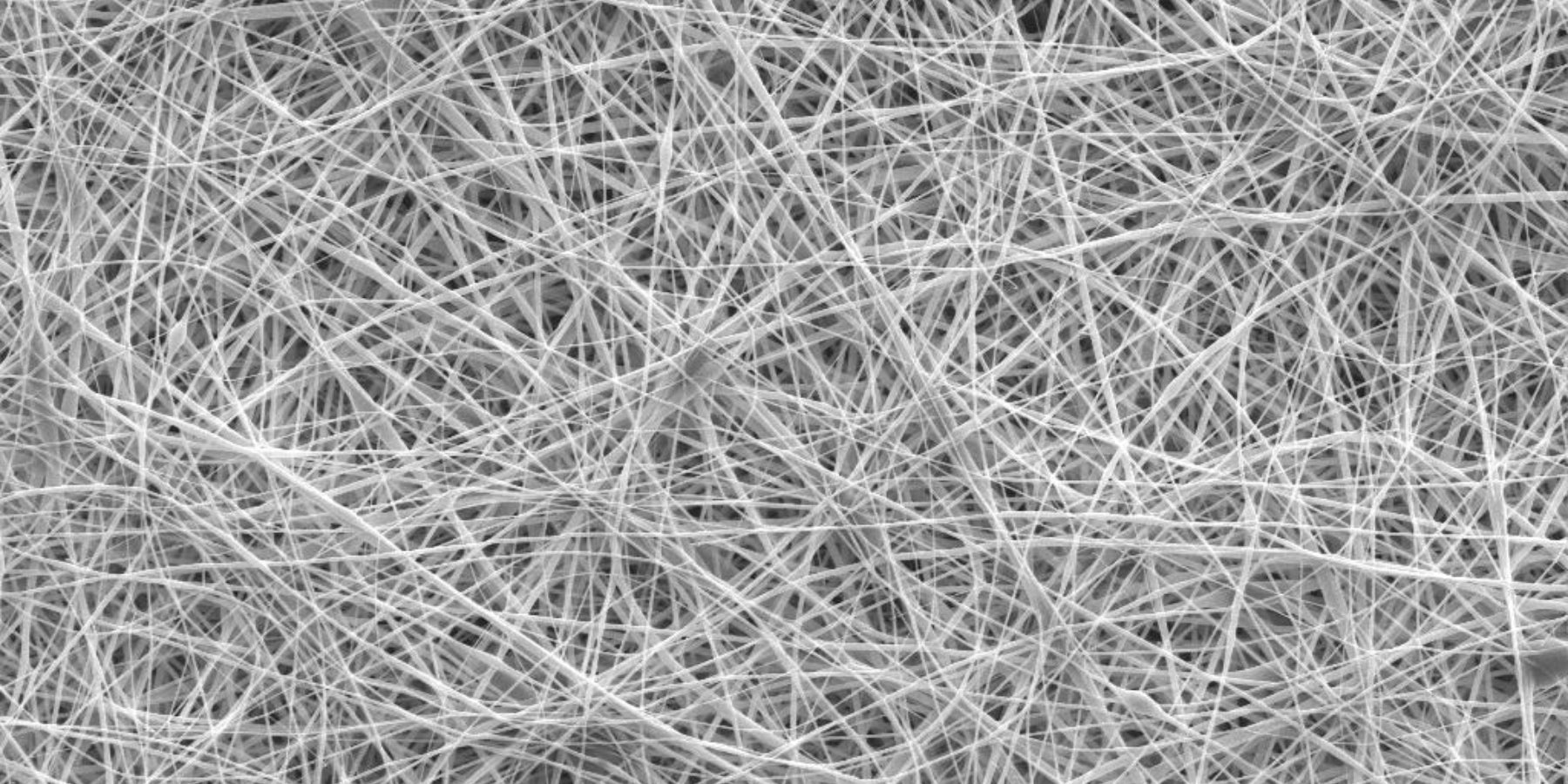 A close-up image showing a chaotic network of thin, white fibers interwoven in random directions against a dark background.