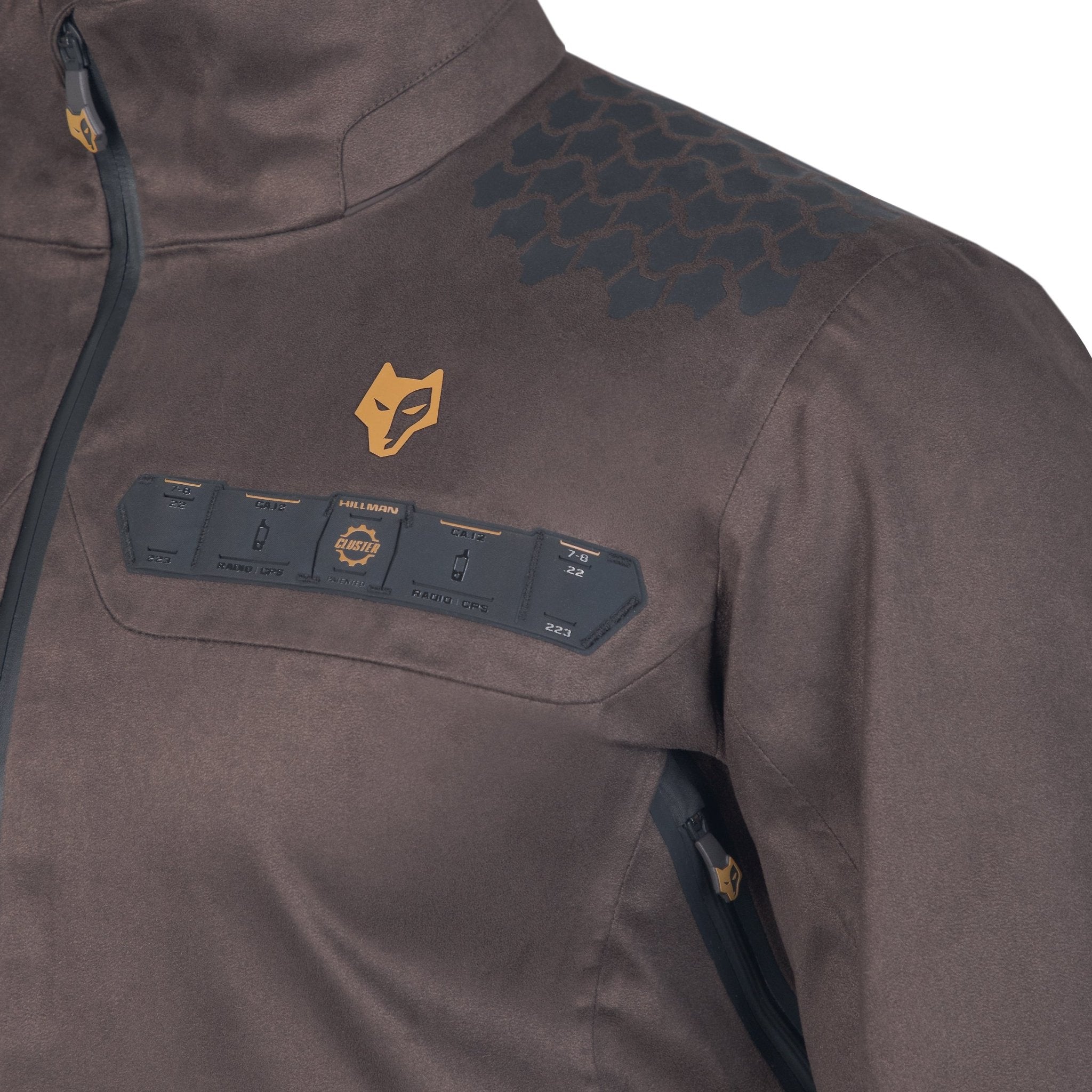 Close-up of a brown 5WL Waterproof Camo Hunting Rain Jacket by HILLMAN GEAR, featuring a stylized animal logo on the chest. The ultra-lightweight design includes fabric patches and black text, with a shiny texture and a diagonal zipper partially visible on the front.